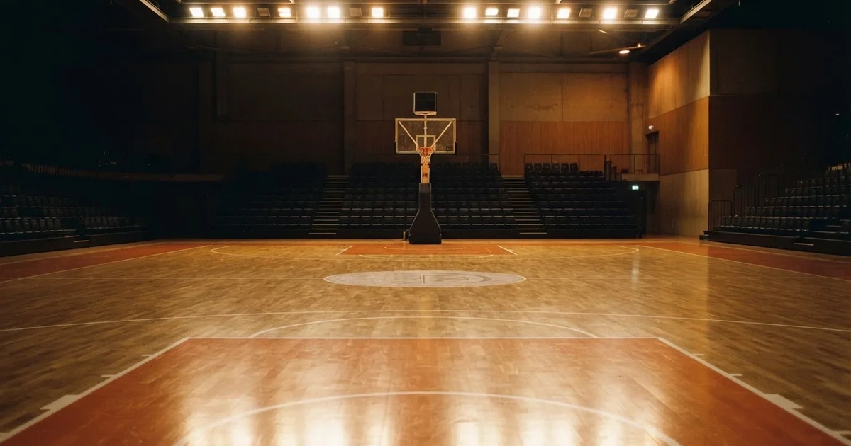 Eine leere Basketballhalle mit glänzendem Parkett und einem Korb im Hintergrund, Licht von Deckenstrahlern spiegelt sich im Boden.
